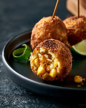 Crispy fried corn croquettes served on a plate with lime wedges and wooden skewers