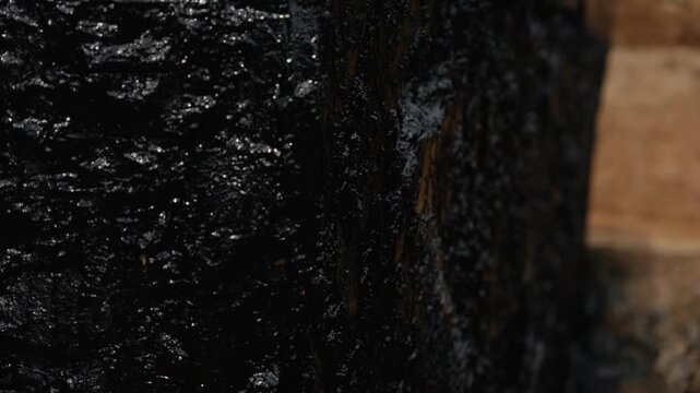 Glistening water cascades down a dark, textured rock surface, with the camera focus gradually shifting to create a beautiful bokeh effect, highlighting the interplay of light and shadow