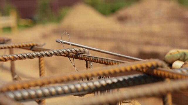 Detailed close up of a builder's hands in protective gloves skillfully tying steel reinforcing bars with wire to create a strong rebar cage for a concrete foundation at a construction site
