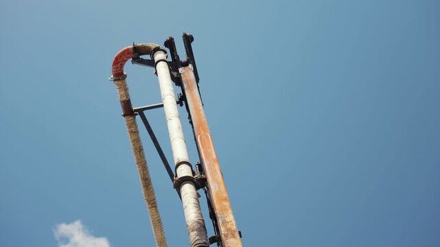 Hydraulic concrete pump boom arm slowly extends upwards against a clear blue sky, showcasing industrial construction machinery in operation at a building site during a sunny day