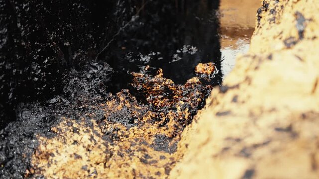 Dense, black crude oil slowly bubbling up and seeping from a natural deposit in the earth's surface. A powerful depiction of fossil fuel extraction and the petroleum industry's impact
