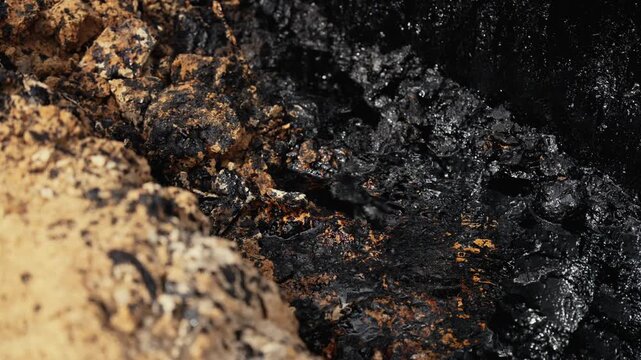 Extreme close up shot capturing thick, black crude oil slowly seeping and spreading over the dry, sandy ground, highlighting the contrast between the pollutant and the natural earth