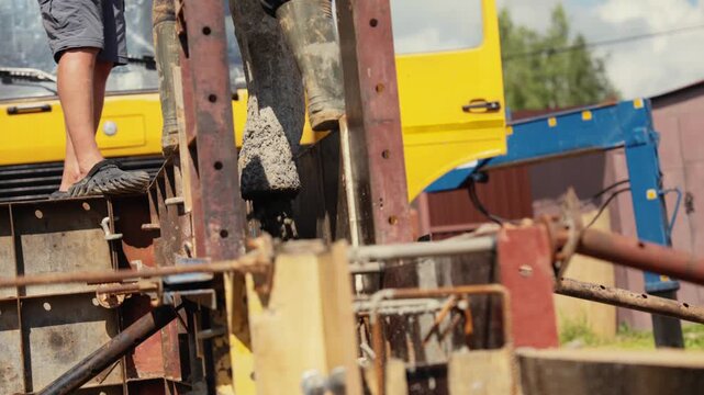 Construction workers pouring liquid concrete from a pump truck hose into a wall formwork, creating a solid foundation for a new building during a sunny day at the construction site