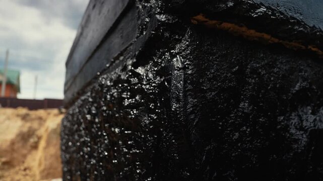 Close up view of a concrete block foundation wall freshly coated with black bitumen mastic for waterproofing, protecting the structure from moisture at a residential construction site