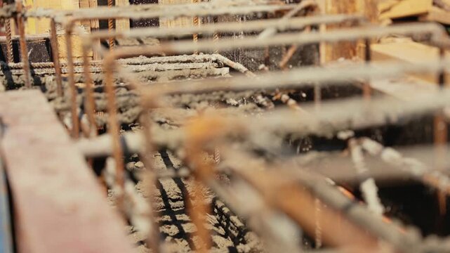 Liquid concrete being poured into wooden formwork with metal rebar cage for reinforcing building foundation, creating a strong and stable base for new construction on a sunny building site