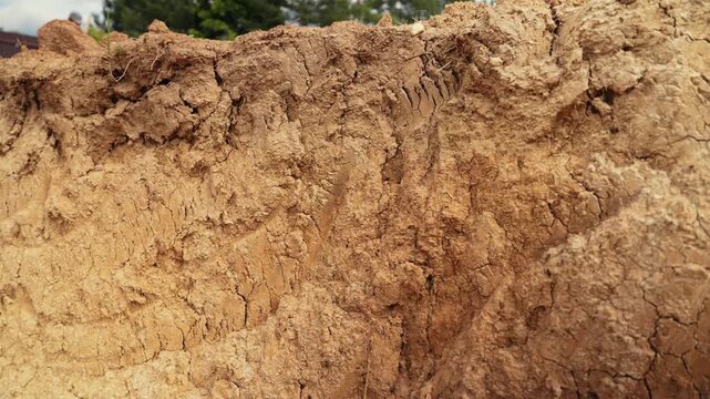 Close up view of a soil cross section revealing layers of dry, cracked earth and clay, showing the ground's texture and composition from an excavation site with visible shovel marks