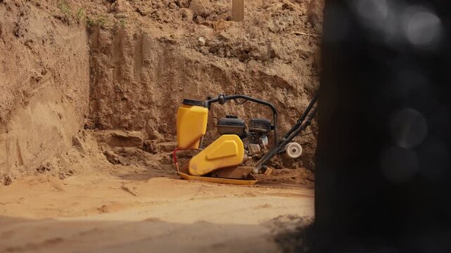 Heavy duty vibratory plate compactor machine leveling sand at a construction site, preparing the ground for the foundation of a new building, shown in a detailed slow motion view