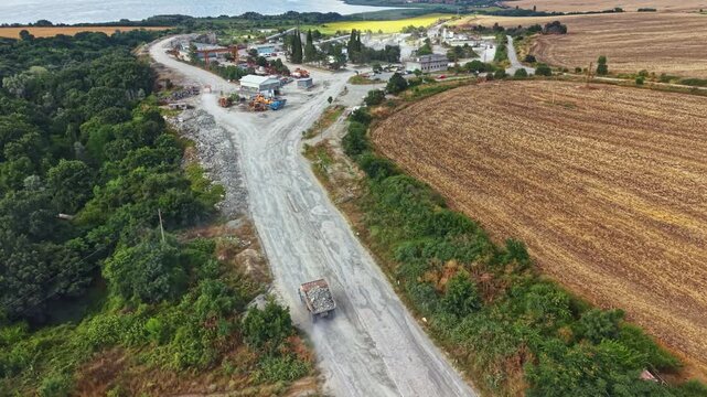 A granite quarry is visible with machinery and buildings near farmland. Dirt roads lead through the quarry site surrounded by green trees and open fields. Bright skies make the scene clear.