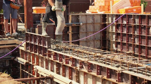 Construction workers pouring liquid concrete into a steel rebar reinforced formwork using a concrete pump hose during the foundation building phase of a new residential home project