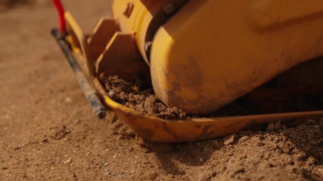 Close up view of a vibratory plate compactor leveling sand on a construction site, with dust particles rising from the powerful machine vibrations during the soil compaction process