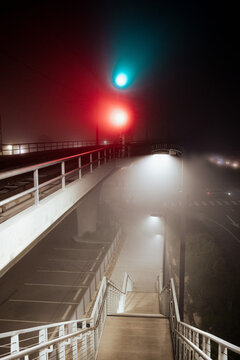 An eerie scene featuring a fog-enshrouded overpass, highlighted by vibrant red and green signal lights, instilling a sense of anticipation in the atmosphere.