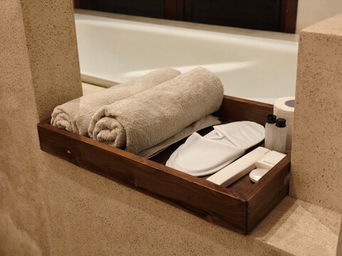 Rolled towels and slippers on a wooden tray beside a hotel bathtub