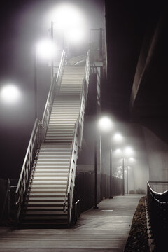 A minimalist photograph of a stairway illuminated by lights, set against a mysterious fog, merging urban architecture with enchanting visual experiences.