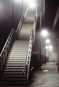 A striking image of an elevated stairway surrounded by fog and lights, creating a mood of solitude and introspection in an enchanting urban environment.