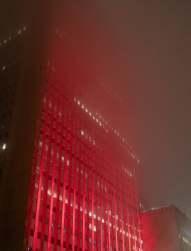 A dramatic image of the misty Chicago skyline, bathed in a glowing red hue, evokes a sense of mystery and urban allure on a foggy night in the heart of the city.