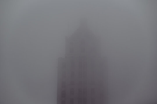 A foggy view of urban architecture, where the top of a tall building disappears into the mist, creating a mysterious and moody atmosphere that evokes curiosity.