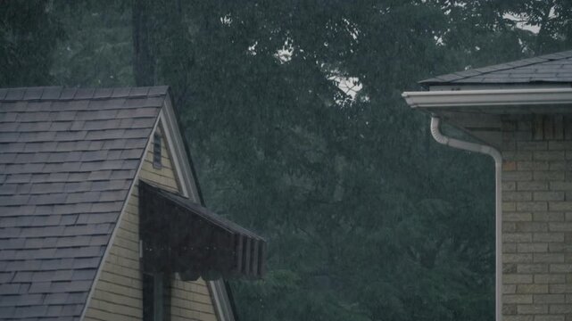 Dramatic slow motion rainfall striking the roofs, gutters, and awnings of neighboring suburban homes during a heavy summer rainstorm. 15275  
