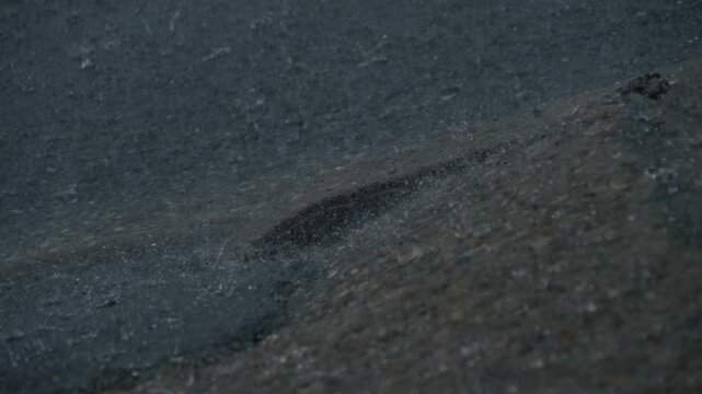 Close-up slow motion view of heavy rainwater flowing along a residential street curb during an intense downpour, highlighting stormwater runoff and drainage. 15277  