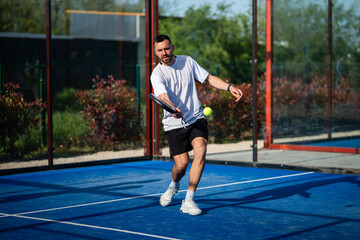 Obraz premium Male padel player hitting a yellow ball on blue court