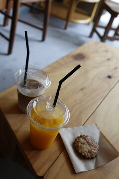 カフェ店内のドリンクとクッキー。オレンジジュースとカフェオレ。木製テーブル