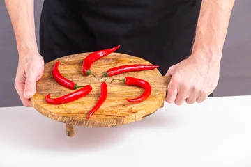 Close-up view of red chili peppers laid out on a cutting board in the hands of a male cook, selective focus © rustamank