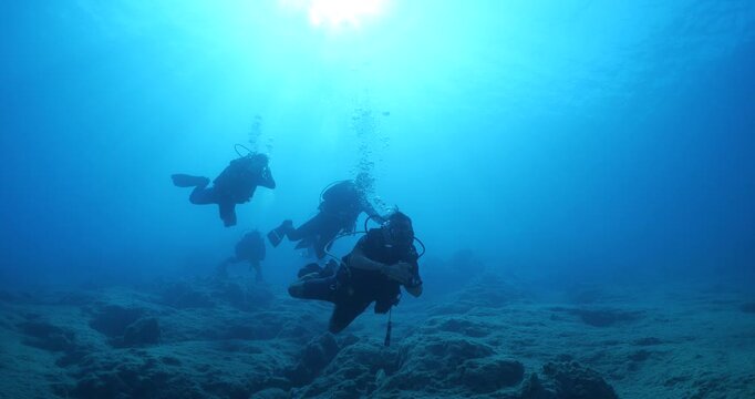  scuba divers exploring around a reef underwater deep blue water big rocks and bubbles ocean scenery 