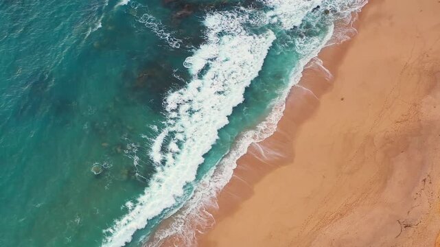 Drone captures a top down perspective of Atlantic waves rolling across a sandy shoreline with vibrant blue water and natural coastal patterns.