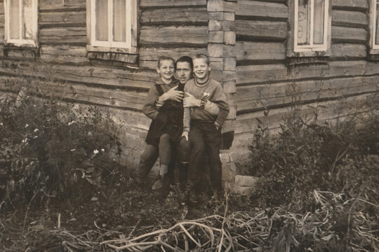Soviet village children beside wooden izba with older brother father outdoors