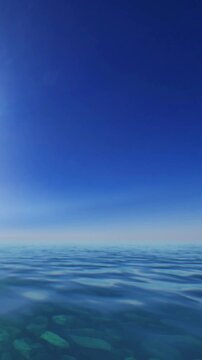 The scene shows clear water with gentle waves reflecting sunlight. The sky is bright with a gradient of blue. The view suggests a coastal area under midday light with no visible land.