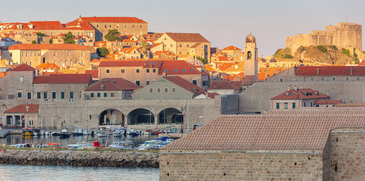Historic stone buildings, harbor and medieval fortifications in Dubrovnik Old Town, Croatia, illuminated by warm sunrise light.