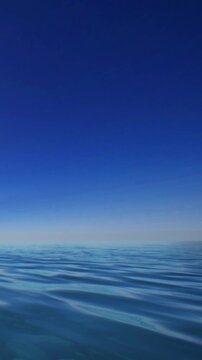 The scene shows water at a beach with gentle waves. A blue sky spreads above with minimal clouds. It is a sunny day, making the water shimmer under the sunlight.