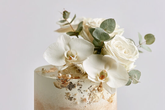Elegant wedding cake featuring white orchids, roses, eucalyptus and gold leaf. Luxury bakery creation isolated on a pure white background for bridal celebrations and premium stock imagery.