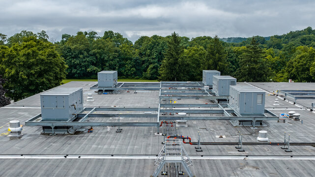 Industrial, commercial HVAC equipment on steel dunnage, and pipes on gray roof.