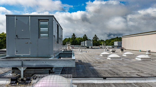 Industrial, commercial HVAC equipment on steel dunnage, and pipes on gray roof.