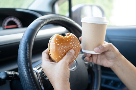 Asian lady holding ice coffee and bread bakery food in car dangerous and risk an accident.
