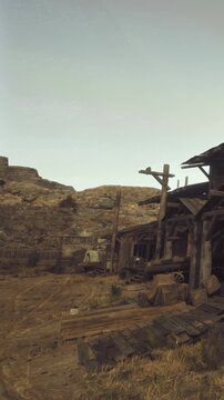 Wooden buildings stand in an old western town under a clear sky. Rocky hills surround the area, creating a rugged landscape. This scene shows life in the past, illustrating abandoned structures.