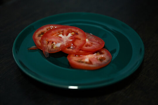 fresh red tomato slices on green plate close up, raw organic tomato round slices on dark wooden table background, fresh healthy food ingredient display with copy space