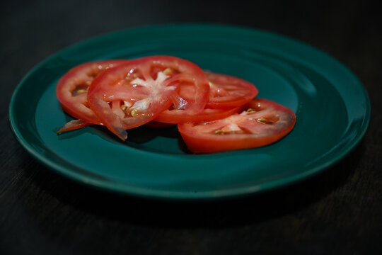 fresh red tomato slices on green plate close up, raw organic tomato round slices on dark wooden table background, fresh healthy food ingredient display with copy space
