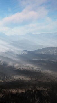 The scene shows a wide view of mountains and valleys in the distance. Clouds cover some areas while sunlight shines on parts of the terrain below. The sky is blue and clear.