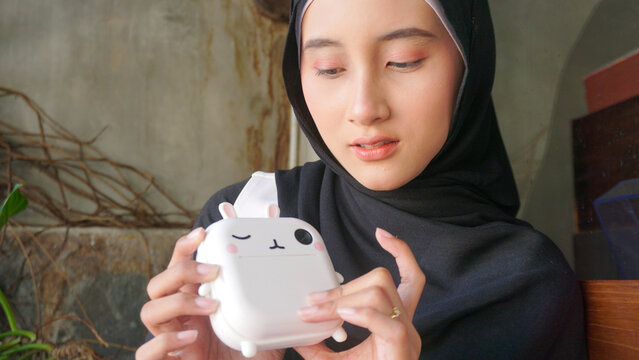 woman's hands holding a cute bunny-shaped portable mini thermal printer and tearing off a freshly printed black and white receipt paper photo.