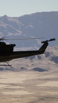 A helicopter moves across a clear blue sky above snow covered mountains. The landscape shows a vast expanse of white terrain and rugged peaks in the background.