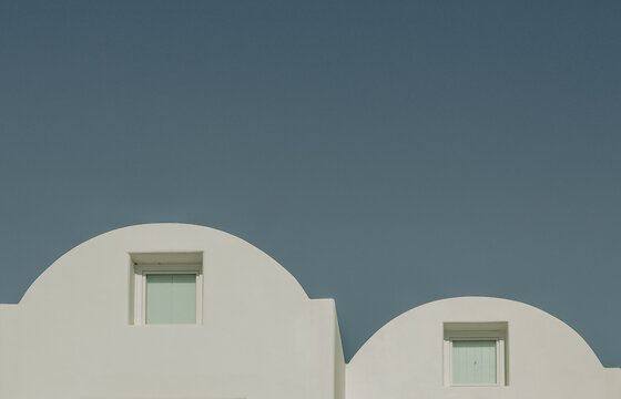 Smooth white domes and pastel windows stand against a deep blue sky in Santorini, Greece, showcasing the clean geometry and timeless elegance of Cycladic architecture.