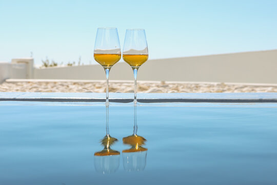 Two glasses of Greek orange wine reflect in the pool under bright Mediterranean light in Santorini, Greece, evoking calm and coastal elegance.