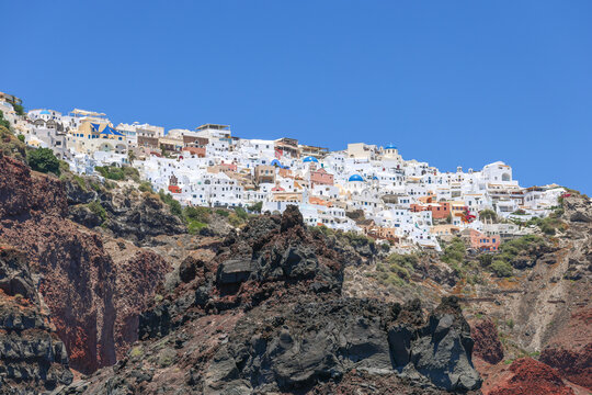 The whitewashed village of Oia perches on volcanic cliffs above the Aegean Sea in Santorini, Greece, glowing under the bright Mediterranean sun.