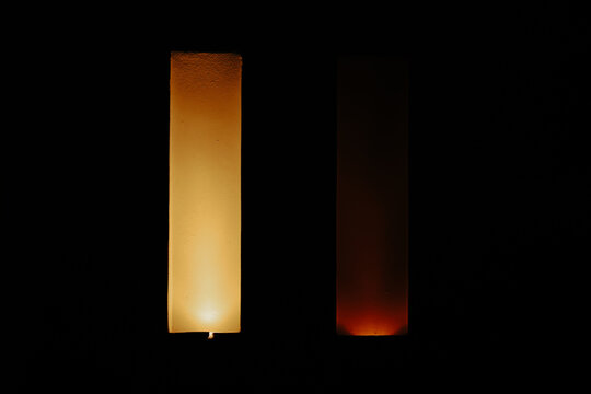 Two vertical panels emit warm yellow and orange light against a dark background, creating a minimalist composition of color and contrast.
