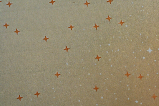 Macro shot of orange four-pointed stars and white specks on paper texture