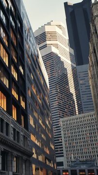 A view of tall buildings reflecting light from the setting sun. The scene shows a mix of modern architecture and older structures. The street is narrow, creating an urban atmosphere.