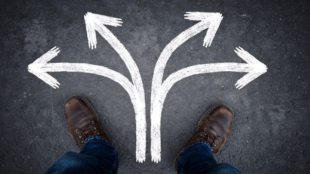 Person standing at a fork in the road with three arrows pointing in different directions on asphalt decision direction lifestyle motivation conceptual opportunity thinking navigation planning