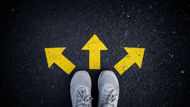Person standing before three painted yellow arrows on asphalt pavement representing decision making with direction decision crossroads opportunity navigation movement selection planning