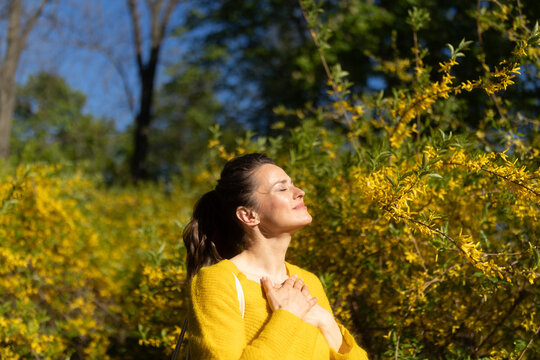 Tilting her head toward the warm sun, a woman in a yellow sweater embodies spring joy. This image captures a moment of deep connection with nature and spiritual reflection.